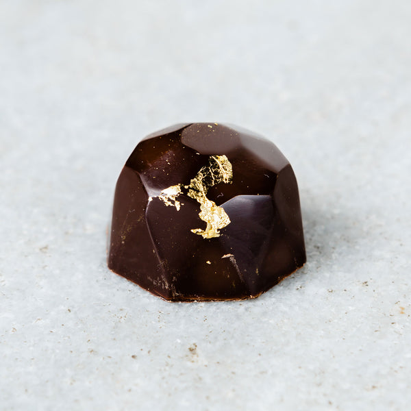 Tempered Chocolate molded dark chocolate champagne truffle topped with gold flakes.