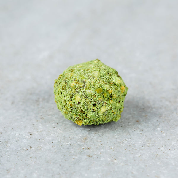 Tempered dark chocolate pistachio matcha truffle topped with chopped pistachios and green matcha powder.