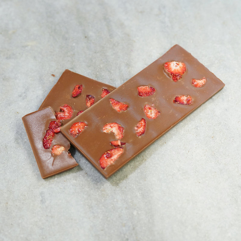 Tempered milk chocolate bar with chopped honey strawberries placed evenly throughout the bar.