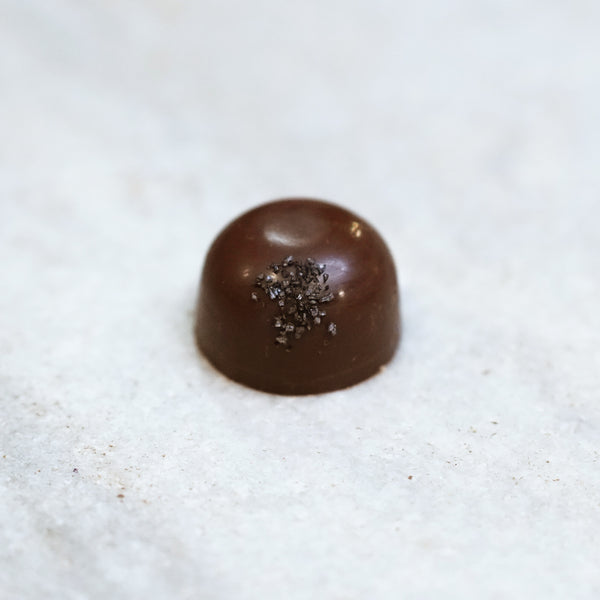 Tempered dark chocolate and Uncle Nearest whiskey truffle topped with black lava salt. 